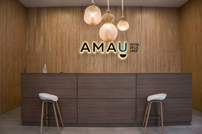 Recepción del AMAU Hotel de la UNLP, con paredes de madera y lámparas colgantes
